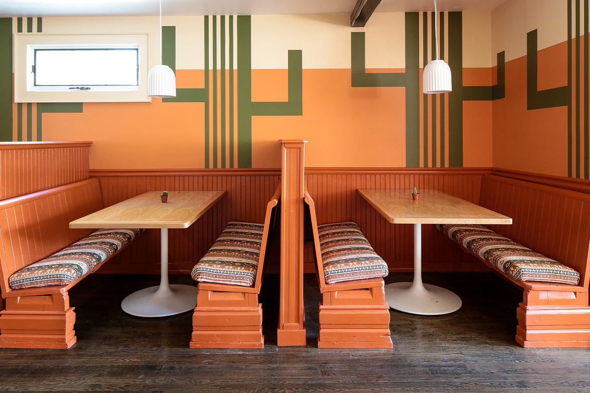 Retro-style diner booths with orange and green geometric wall pattern and pendant lights hanging above wooden tables.