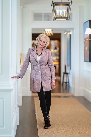 Person in a stylish pink coat and black pants standing in a well-lit hallway.