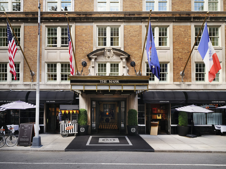 Entrance of a luxury hotel with flags and outdoor dining area on a city street.