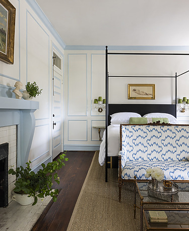 Elegant bedroom with blue and white decor, four-poster bed, patterned settee, fireplace, and a potted plant.