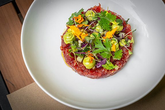 Gourmet dish of beef tartare topped with fresh greens and edible flowers on a white plate.
