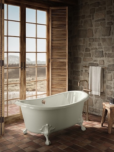 Freestanding vintage bathtub in rustic bathroom with stone walls and large windows overlooking countryside.