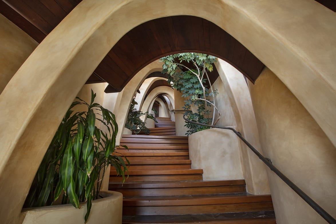 Spiral staircase with wooden steps and indoor plants under curved arches in a modern architectural design.
