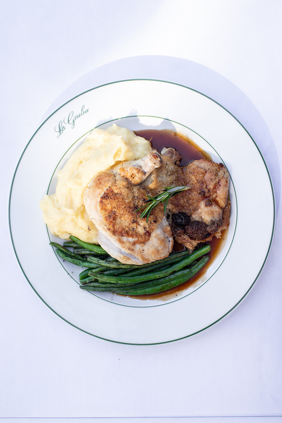 Plate of roasted chicken with mashed potatoes, green beans, and gravy on a white dish with green rim.