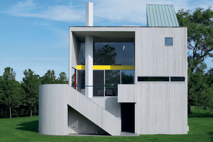Modern two-story house with geometric design, large glass windows, and rooftop skylight, set on a green lawn with trees.