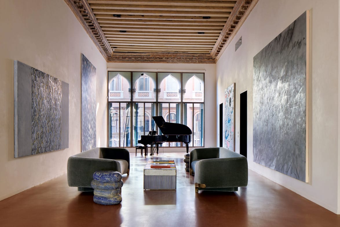 Spacious art gallery with large abstract paintings, modern furniture, and a grand piano near tall windows with arched details.