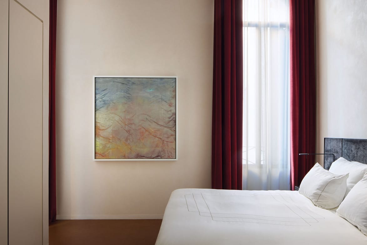 Modern bedroom with minimalist design, featuring a large abstract painting on the wall and red curtains by a tall window.