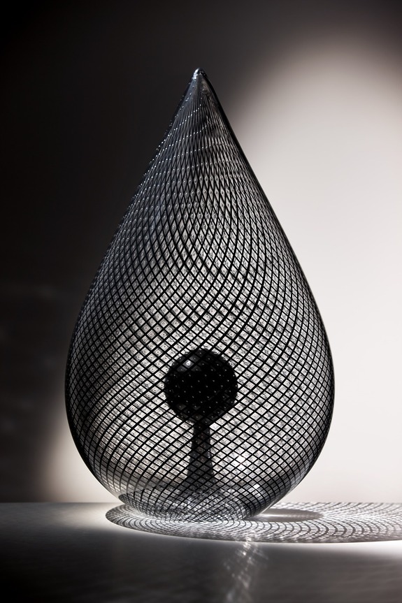 Modern teardrop-shaped wire sculpture with intricate black mesh casting complex shadows on a white surface