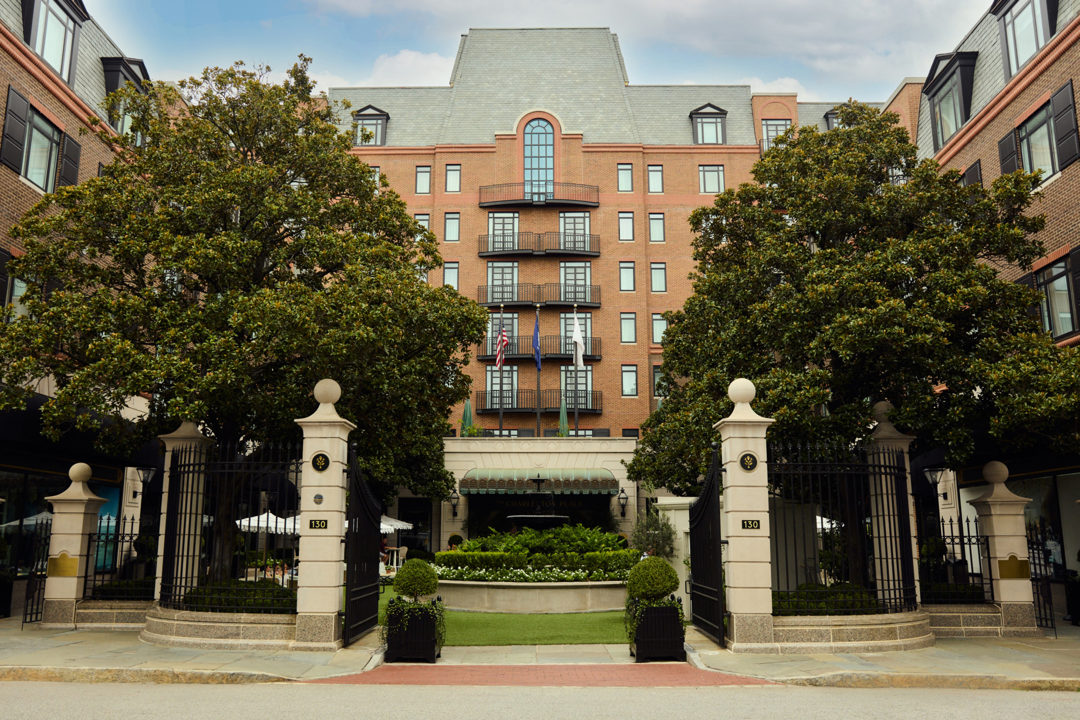 Exterior view of a large brick hotel with trees and a gated entrance during daytime.