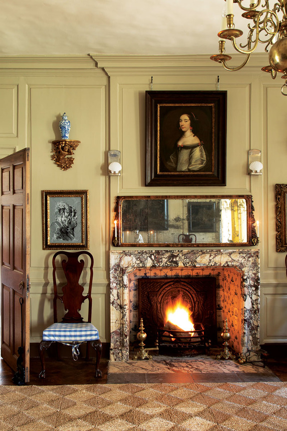 Elegant vintage room with a lit fireplace, antique paintings, wooden chair, and ornate decor.