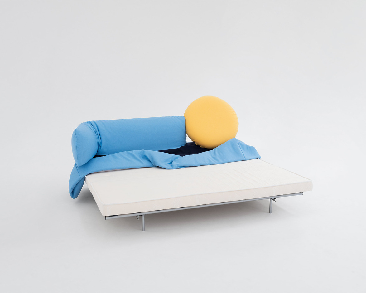 Modern sofa bed with a blue backrest, yellow circular cushion, and a white mattress on a minimalistic gray background.