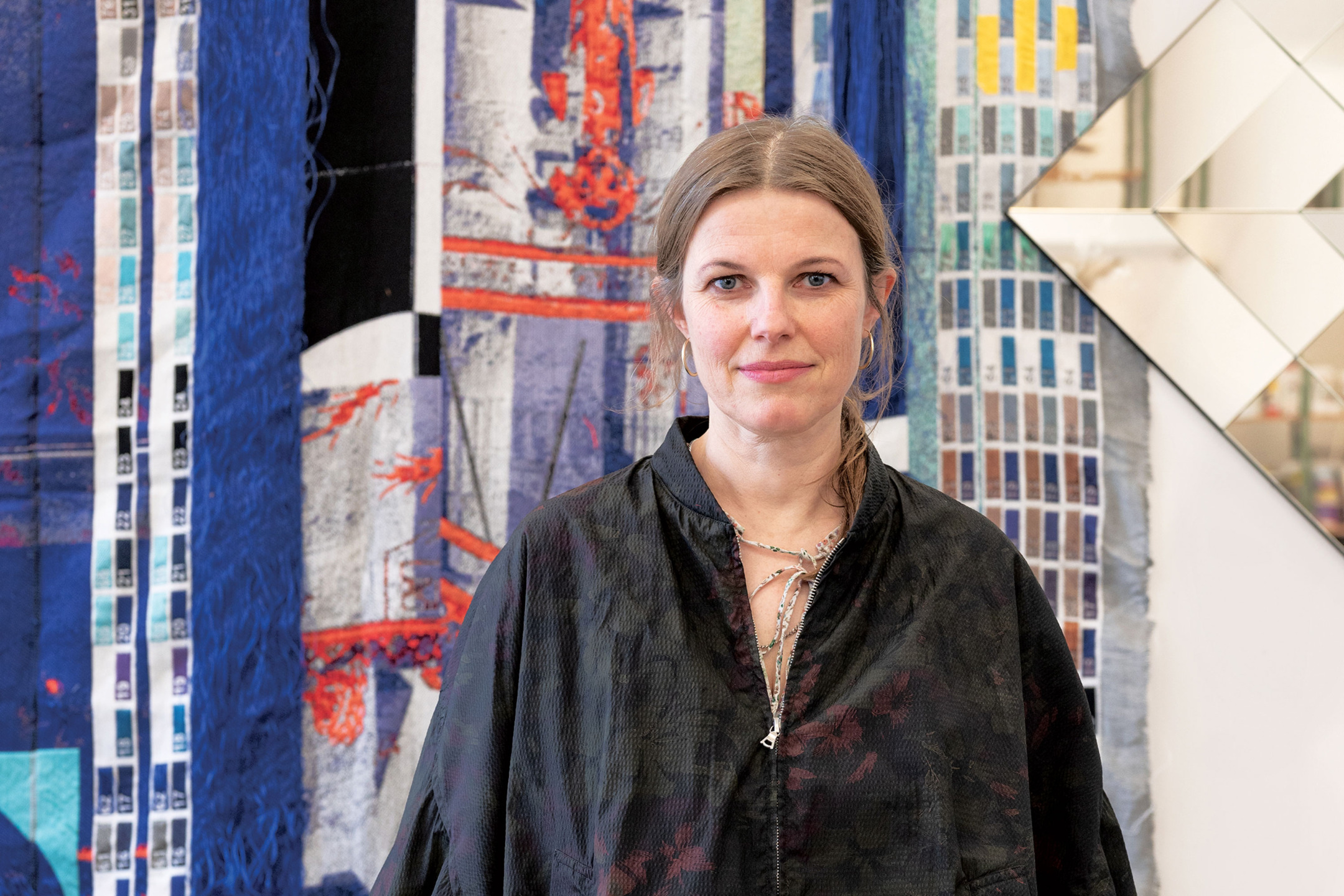 Person standing in front of a colorful abstract artwork, wearing a dark patterned shirt.