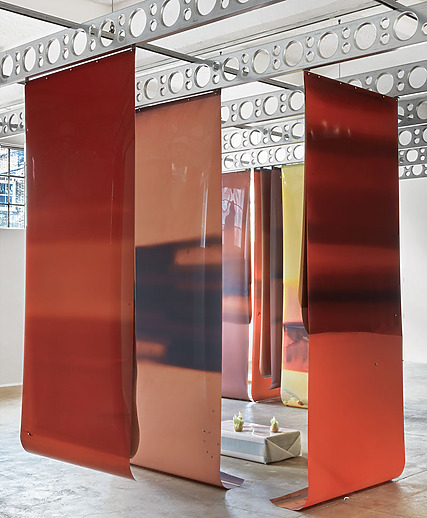 Art installation with large, curved panels in shades of red and orange hanging from a ceiling with circular patterns.