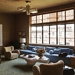 Retro-style living room with a blue sofa, modern lighting, and vintage decor elements, featuring large windows with city view.