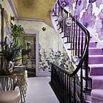 Vibrant staircase with floral wall designs, pink carpet, black railing, and modern lighting fixtures in a stylish home interior.