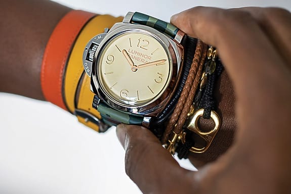 Person wearing a stylish wristwatch with a beige face and leather straps, adjusting the time with their hand.