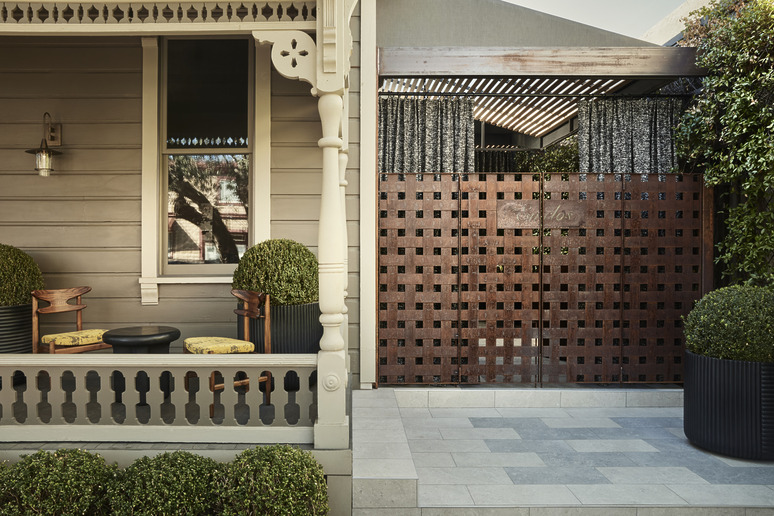Front porch of a traditional home with decorative wooden railing, potted plants, and a patterned wooden gate.