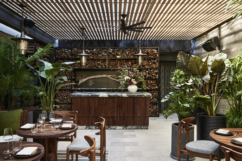 Modern outdoor dining area with wooden furniture, lush green plants, and a decorative wooden ceiling.