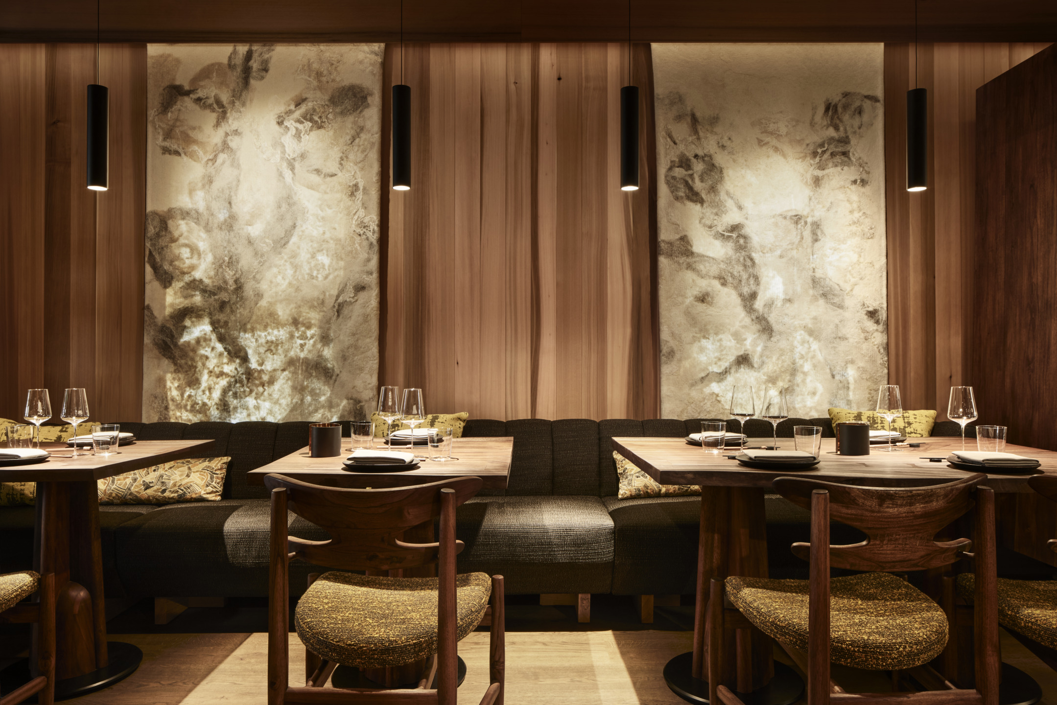 Cozy restaurant interior with wooden tables, cushioned seating, artistic wall decor, and pendant lighting.