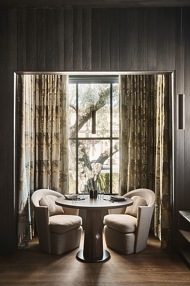 Cozy dining setup with two cushioned chairs and a round table by a window with patterned curtains and wooden flooring.
