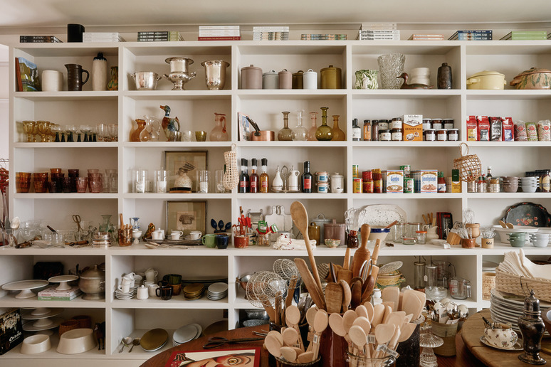 Kitchen shelves filled with various glassware, utensils, canned goods, and decorative items in a well-organized pantry.