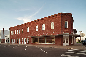 Red brick building at a street corner with large windows and a clear blue sky in the background.