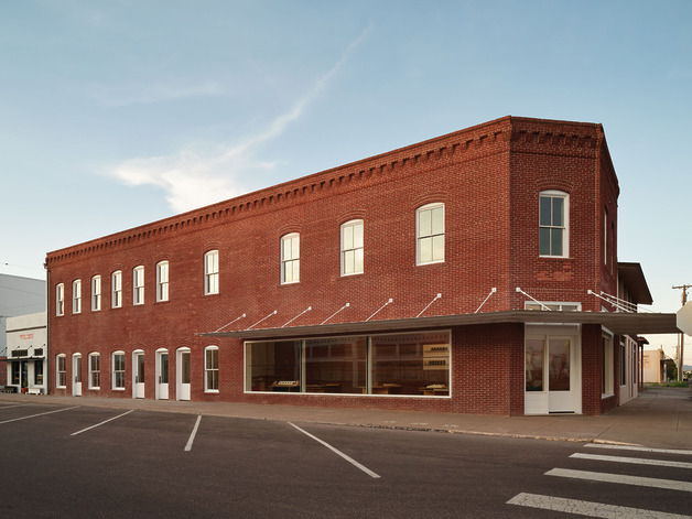 Red brick building at a street corner with large windows and a clear blue sky in the background.