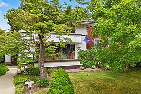 A charming white house surrounded by lush green trees and a neatly trimmed lawn with a stone pathway leading to the entrance.