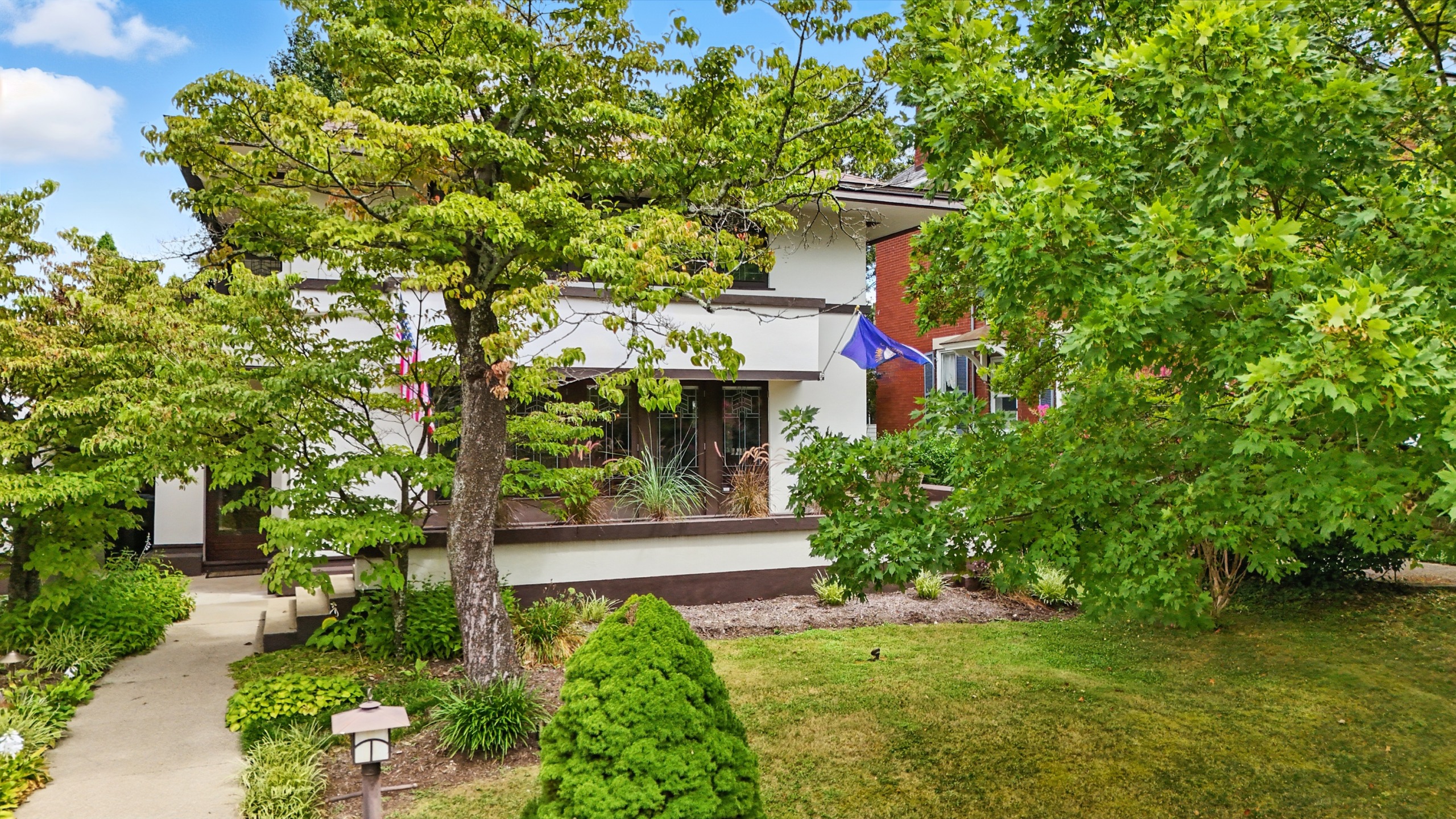 A charming white house surrounded by lush green trees and a neatly trimmed lawn with a stone pathway leading to the entrance.