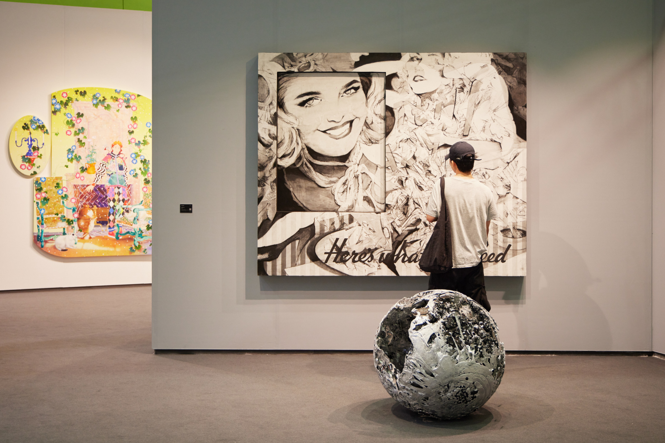 Person viewing comic-style artwork in a gallery with a textured sphere sculpture in the foreground.