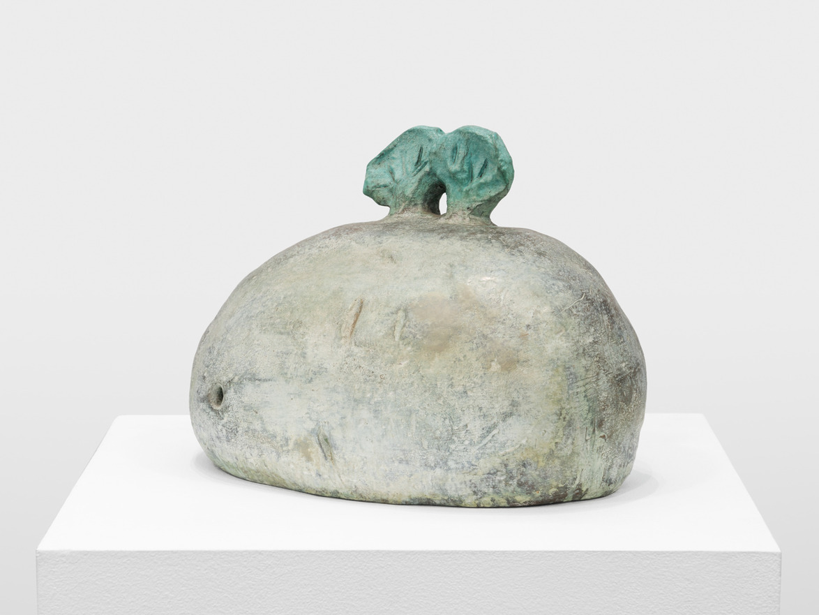 Stone sculpture with a rounded base and two small, abstract shapes on top, displayed on a white pedestal.