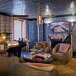 Cozy living room with plush chairs, a fireplace, art on the walls, and a window letting in natural light.