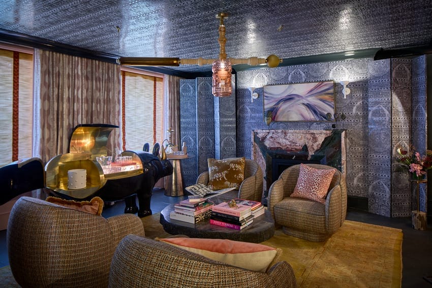 Cozy living room with plush chairs, a fireplace, art on the walls, and a window letting in natural light.