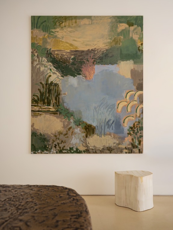 Colorful abstract painting of a landscape with blue water, green foliage, and arches, hanging on a wall above a wooden stool.
