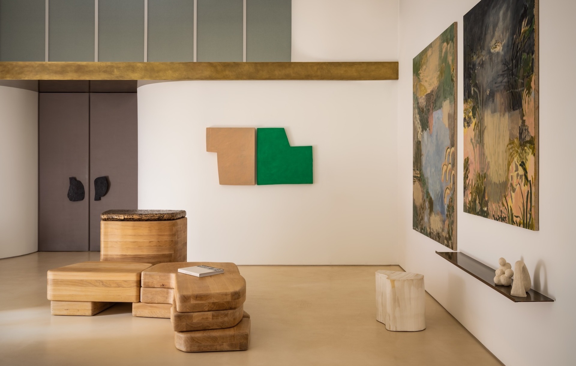 Modern art gallery with abstract paintings, wooden sculptures, and minimalist decor on light-colored walls and floor.