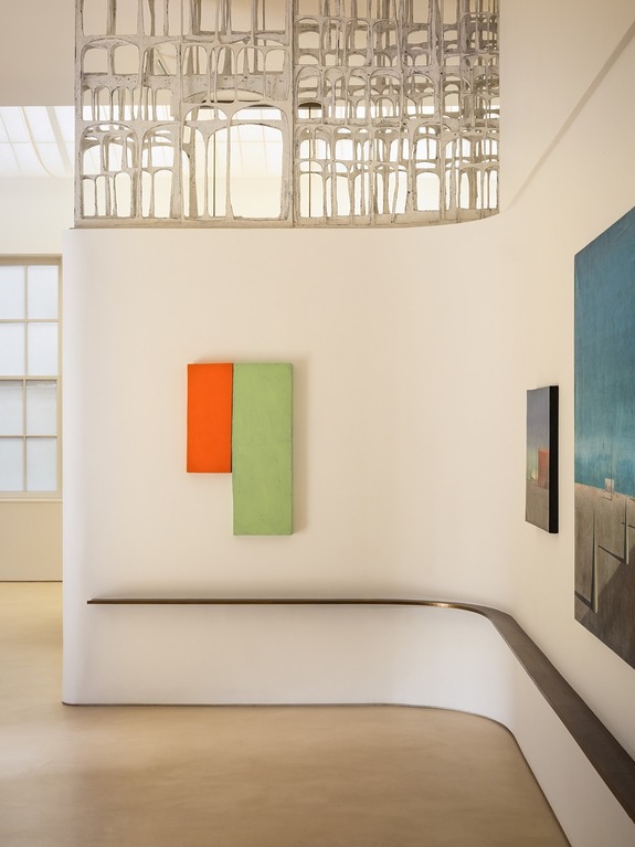 Minimalist gallery corner with abstract art and unique architectural design featuring overlapping chairs in an open ceiling.