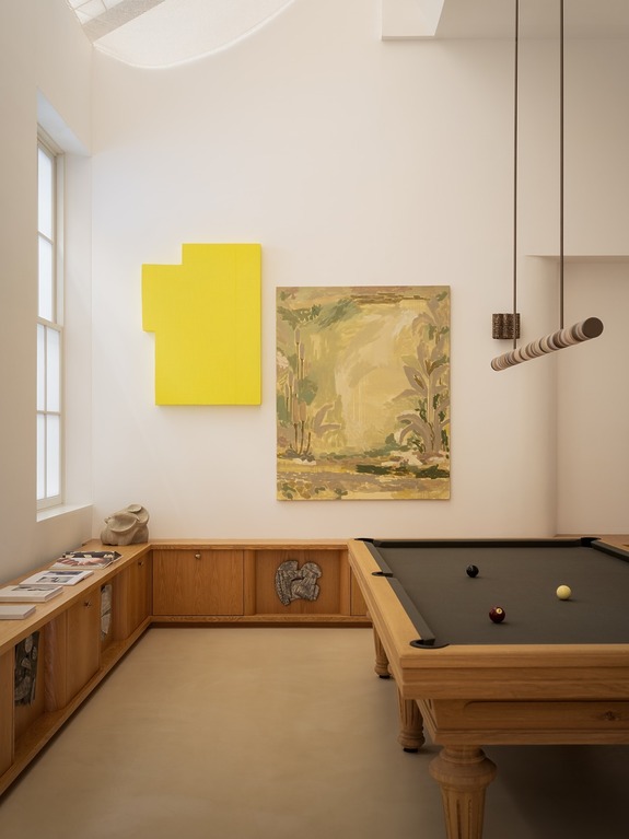 Contemporary room with a billiards table, abstract paintings on the wall, and magazines on a wooden cabinet.