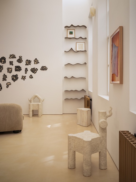 Modern art and sculpture display in a minimalist room with wavy shelves and unique textured chairs.