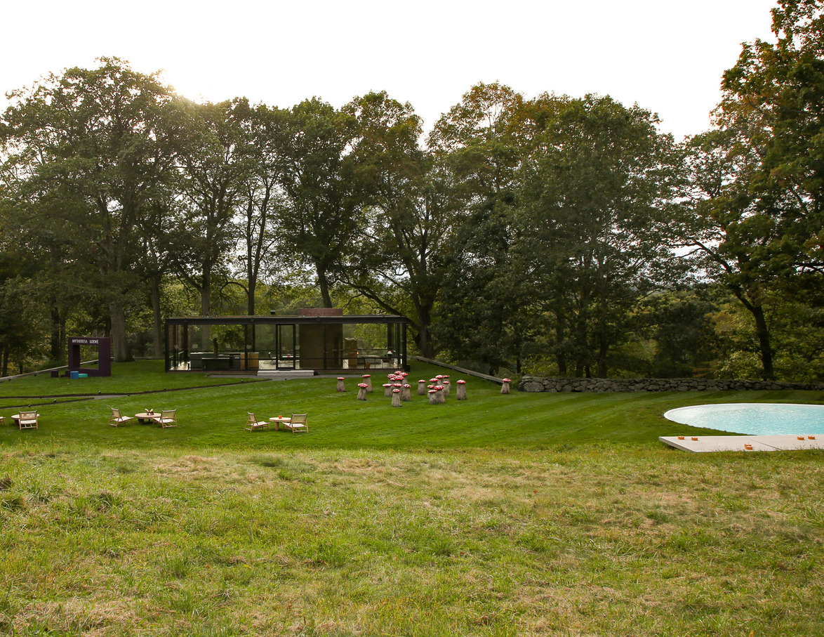 Modern glass building with trees and sculptures on a grassy lawn, overlooking a round pool in a serene outdoor setting