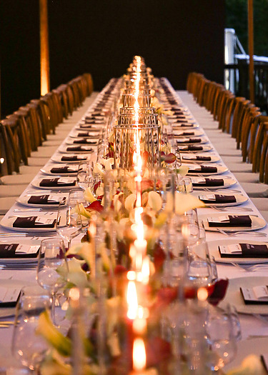 Long dining table with elegant place settings, lit by numerous candles, creating a warm and inviting atmosphere.