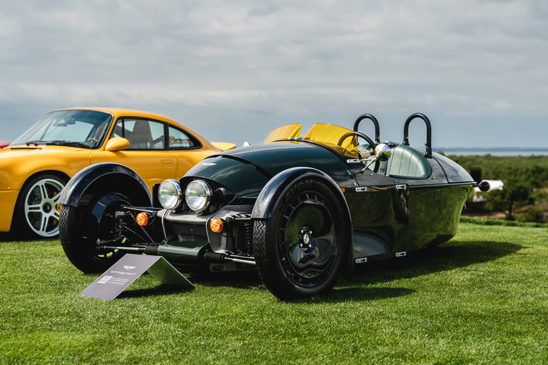 Vintage three-wheeled car with a sleek black design on display next to a bright yellow sports car, parked on grass.