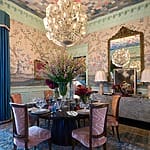 Luxurious dining room with elegant chandelier, floral centerpiece on table, ornate wallpaper, and ornate mirrors.