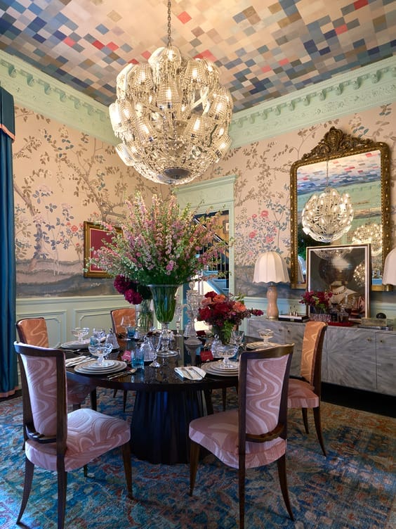 Luxurious dining room with elegant chandelier, floral centerpiece on table, ornate wallpaper, and ornate mirrors.