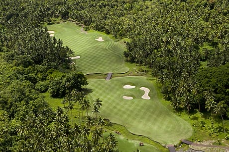 Aerial view of lush golf course with sand traps and abundant palm trees surrounding the fairway.