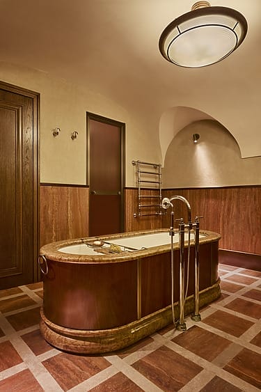 Elegant bathroom with a vintage wooden bathtub, ornate fixtures, and warm-toned walls under soft ceiling light.