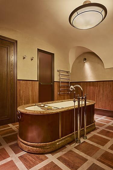 Elegant bathroom with a vintage wooden bathtub, ornate fixtures, and warm-toned walls under soft ceiling light.