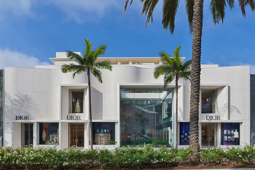Front view of a modern Dior storefront with large glass windows, palm trees, and a clear blue sky in the background.