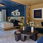 Luxurious modern bedroom with navy walls, stylish decor, and a cozy bed next to a dark wood coffee table and floral accents.