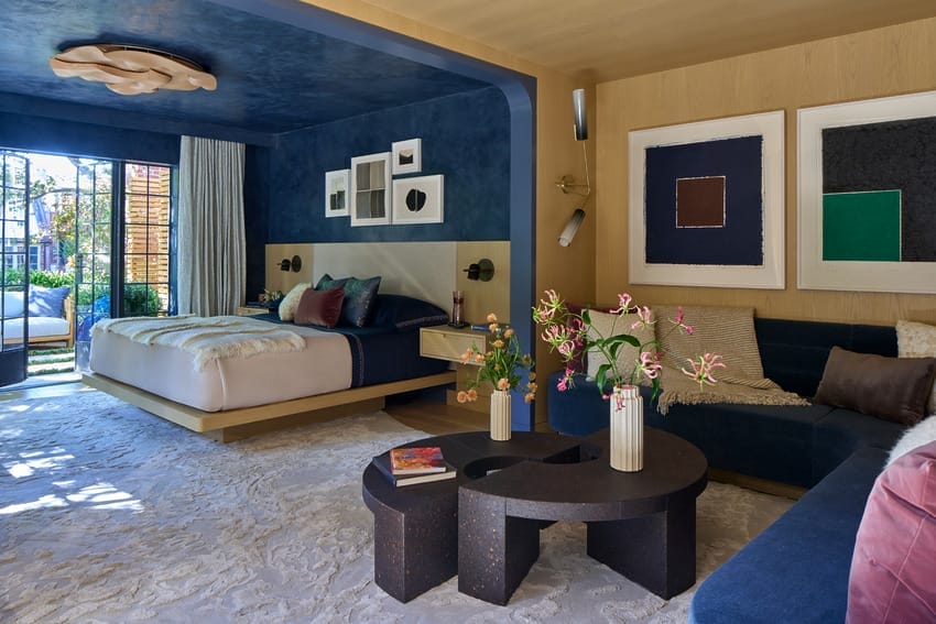 Luxurious modern bedroom with navy walls, stylish decor, and a cozy bed next to a dark wood coffee table and floral accents.