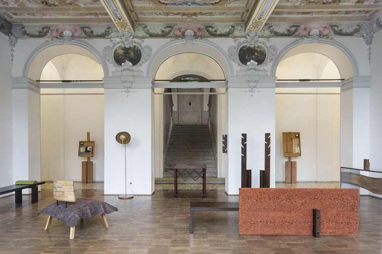 Exhibit of modern furniture in a grand hall with arched windows, ornate ceiling, and a staircase in the background.